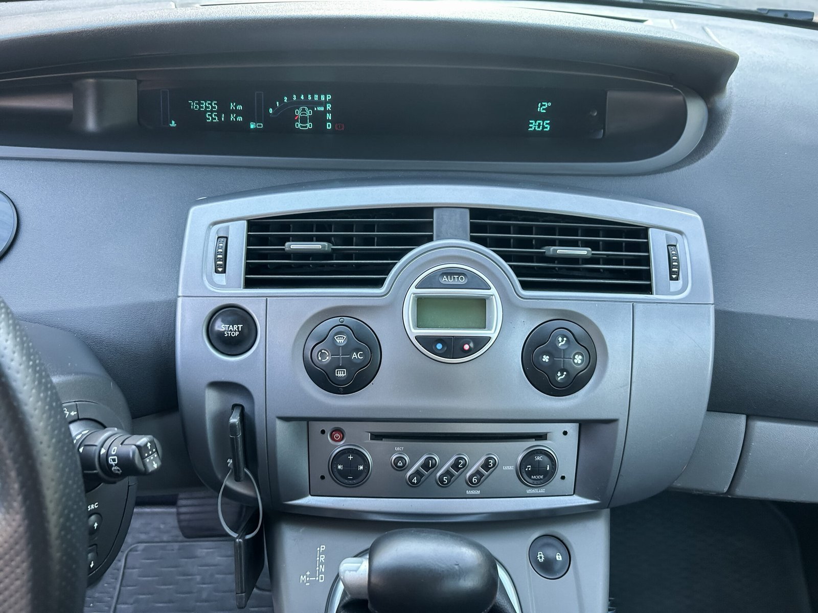 Inside a vehicle, the dashboard displays various digital readings, including temperature and mileage, while climate controls are ready for use on a bright, sunny afternoon.